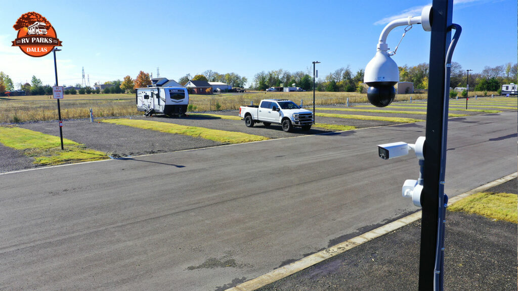 Security camera on a pole overlooking gravel RV sites with a travel trailer and a pickup truck