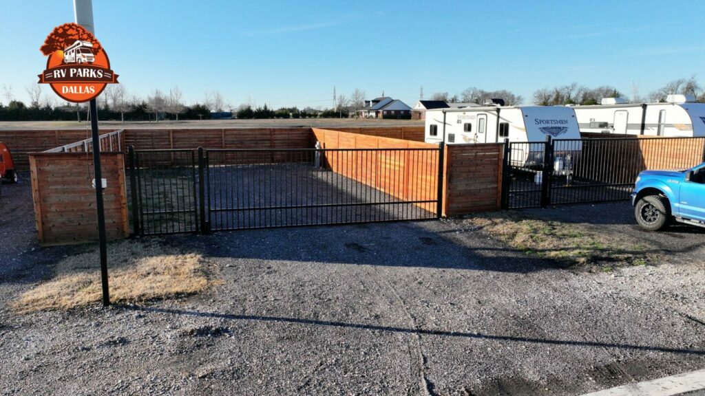 Empty RV lot enclosed by a wooden privacy fence with black metal gates